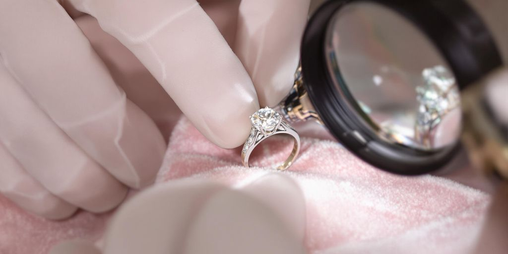 Mains évaluant une bague diamant sur fond en velours sombre.