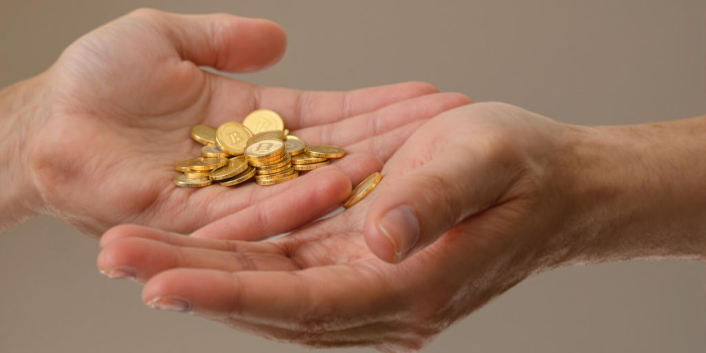 Main tendant des pièces d’or à une autre main ouverte.