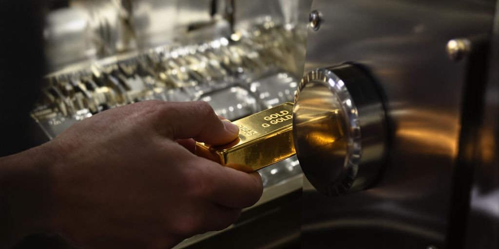 Main tenant une barre d'or devant un coffre-fort ouvert