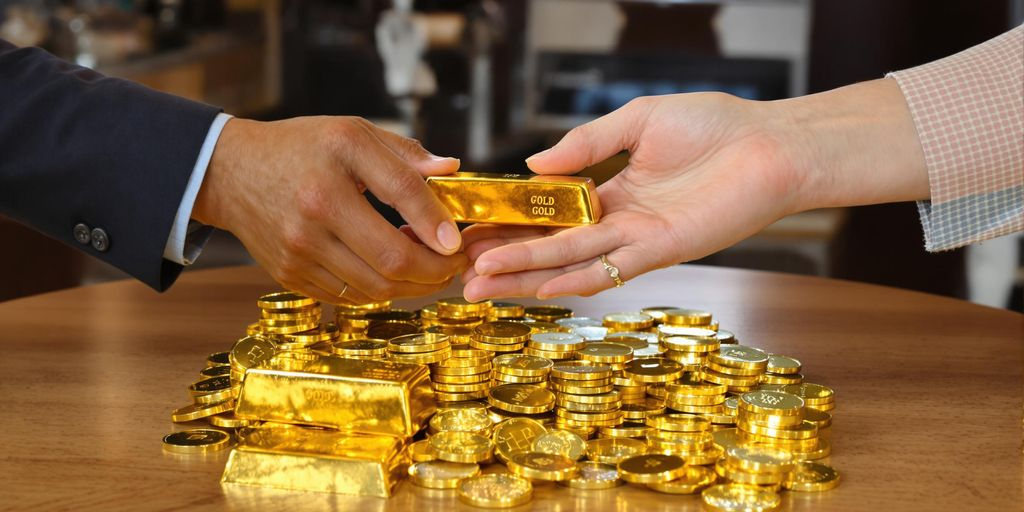 Deux mains échangent des lingots et pièces d'or brillants.