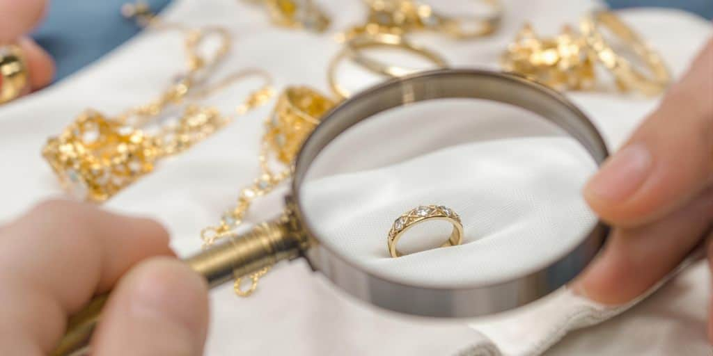 Main tenant une loupe examinant une bague en or sur tissu.