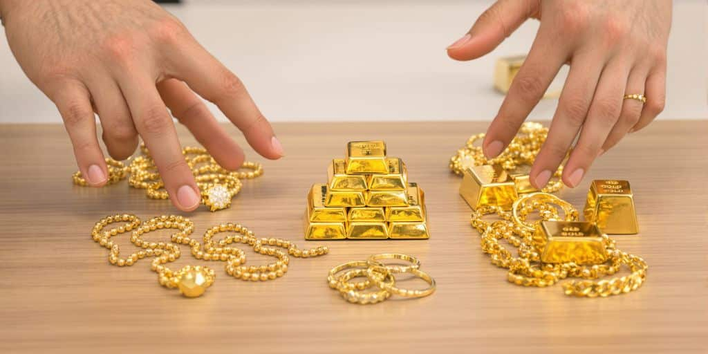 Deux mains tendues vers des bijoux et lingots en or.