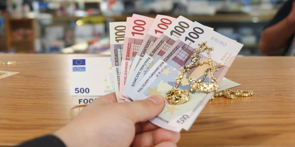 Main posée sur billets d'euro et bijoux en or