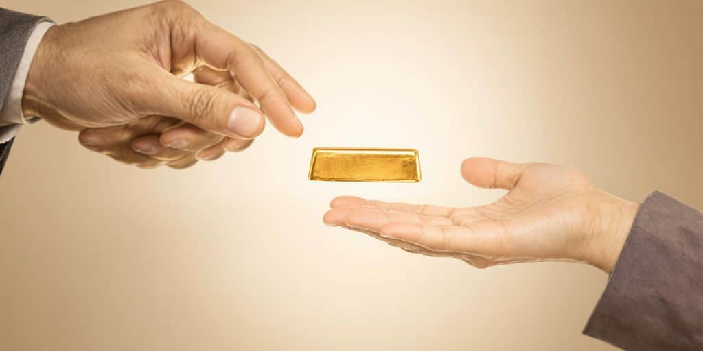 Deux mains transmettent un lingot d’or à d’autres mains.