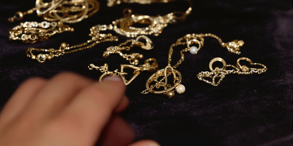 Main tendue vers des bijoux en or sur velours sombre.
