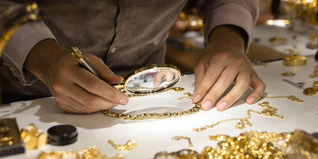 Bijoutier analysant un collier en or avec une loupe.