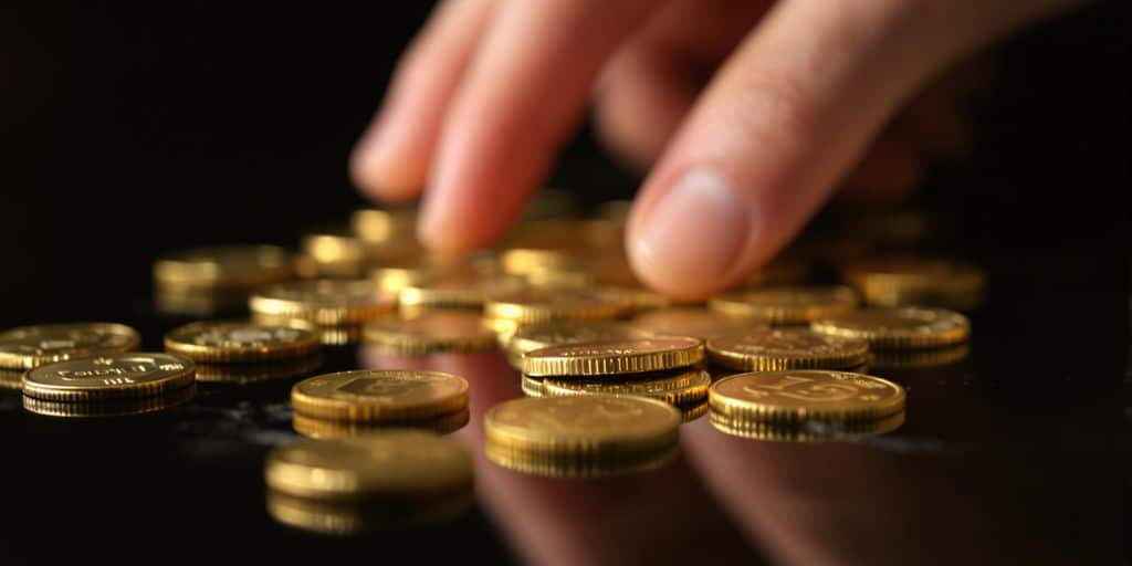 Main posée près de pièces d'or sur une table sombre.