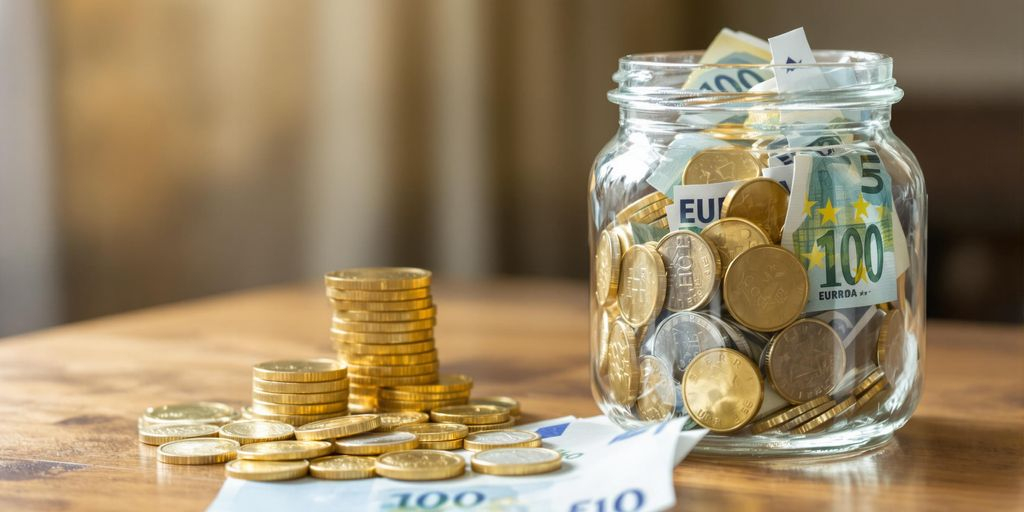 Pièces d'or à côté d'un bocal de billets d'euros