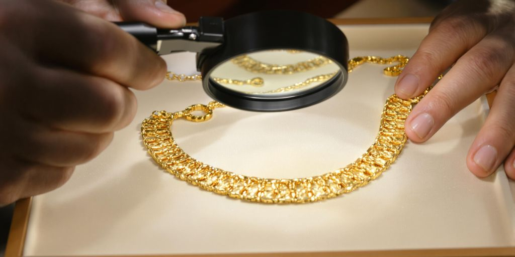 Bijoutier examinant un collier en or avec une loupe.