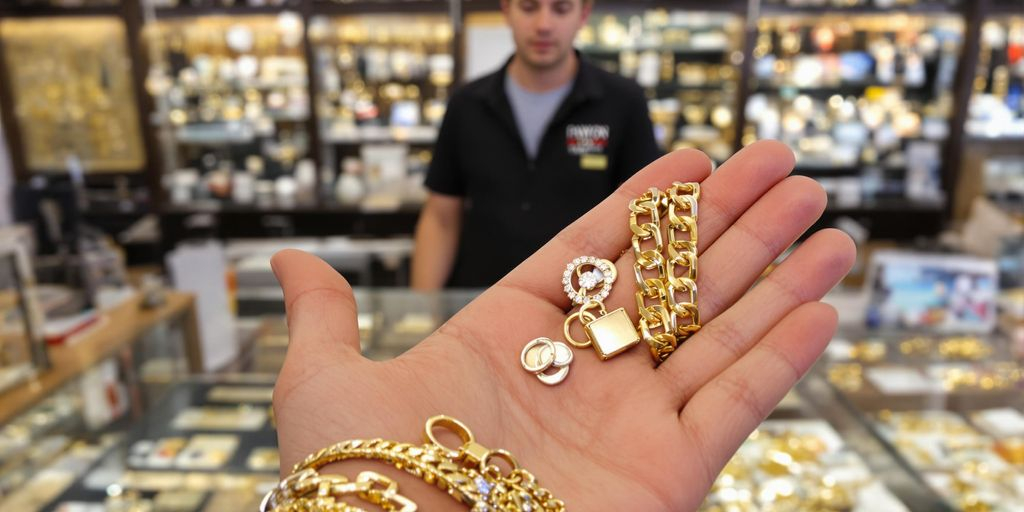 Main tendant des bijoux en or devant un comptoir de prêteur