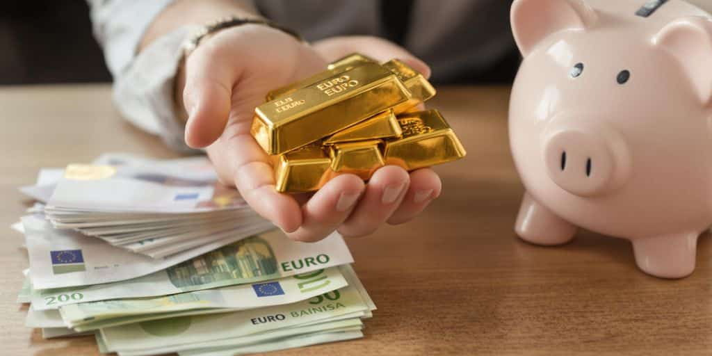 Main tenant des lingots d'or et billets sur une table.