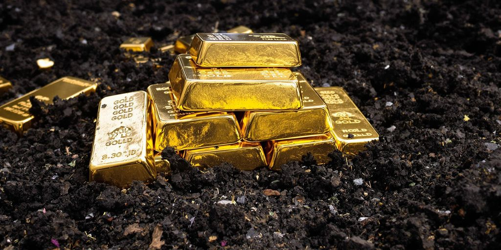 Lingots d’or sur terre sombre avec mains de mineurs visibles.
