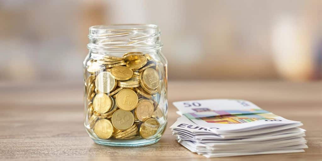 Bocal de pièces d’or et billets euros sur une table