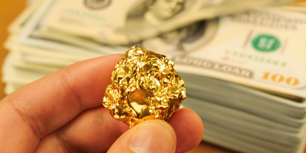 Main tenant une pépite d'or, face à des billets de dollar.