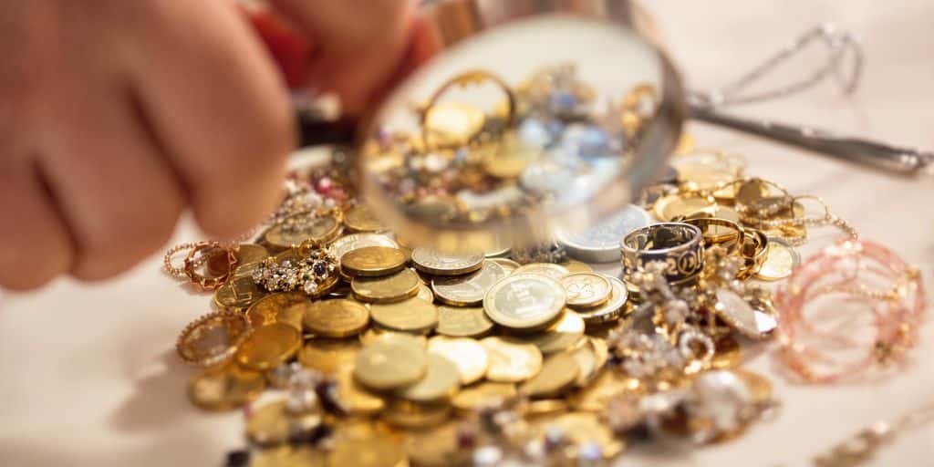 Main tenant une loupe au-dessus de pièces d'or et de bijoux.