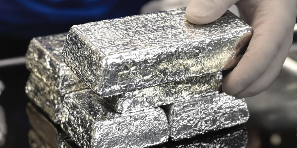 Lingots de palladium gris-blanc empilés, inspectés par une main.