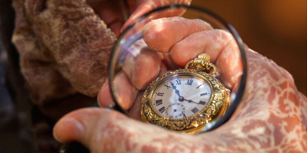 Main tenant une loupe au-dessus d'une montre de poche dorée.