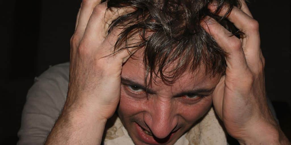 Personne stressée par ses dettes, mains sur la tête, ambiance sombre.