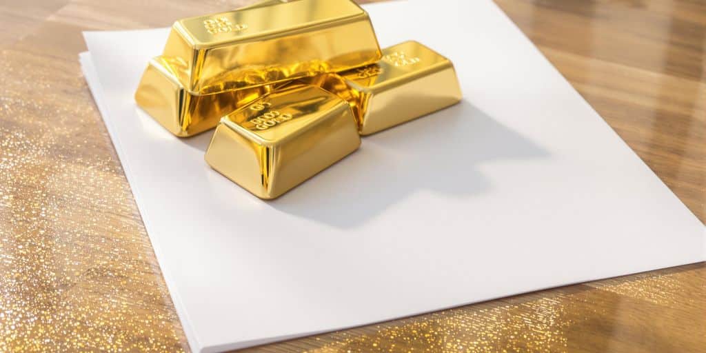 Barres d’or brillantes posées sur feuilles blanches sur surface boisée