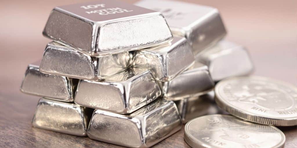 Lingots d'argent empilés dans des mains tenant une pièce.