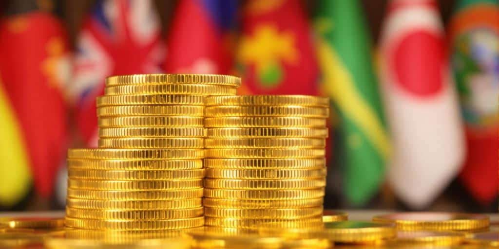 Pièces d'or empilées devant des drapeaux de pays différents.