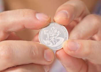 Main tenant une loupe au-dessus de pièces d'argent.