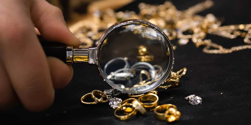 Main tenant une loupe examinant des bijoux en or.