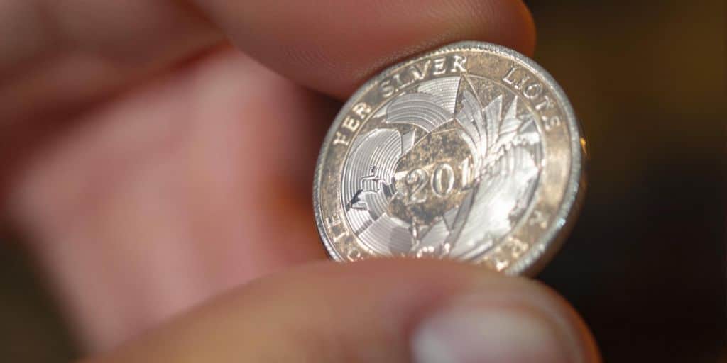 Main d'une personne tenant une pièce d'argent brillante.