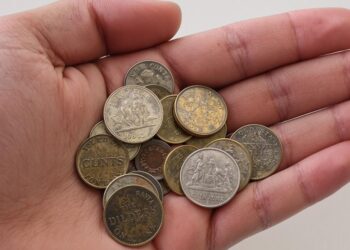 Une main tenant plusieurs pièces de monnaie anciennes.