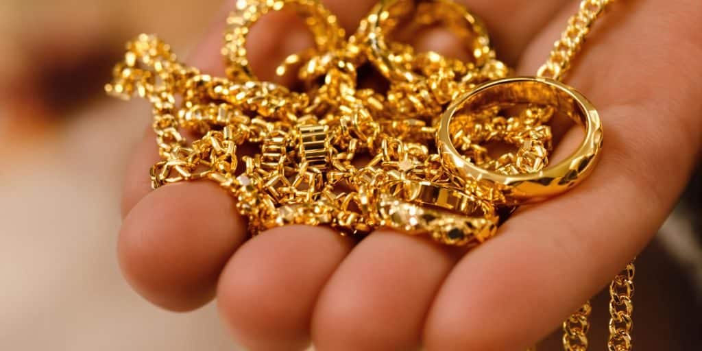 Une main tenant des bijoux en or scintillants sur un fond neutre.