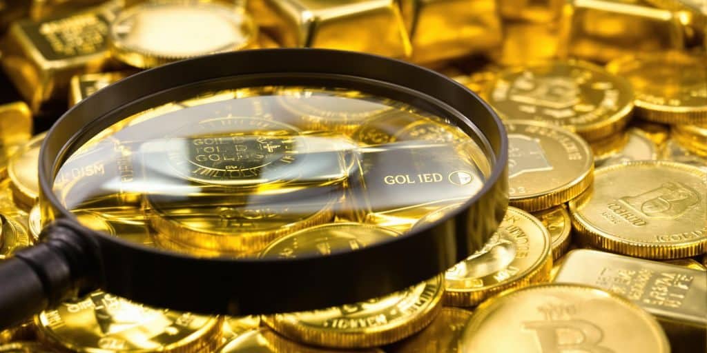 Lingots d'or et pièces d'or brillants près d'une loupe.