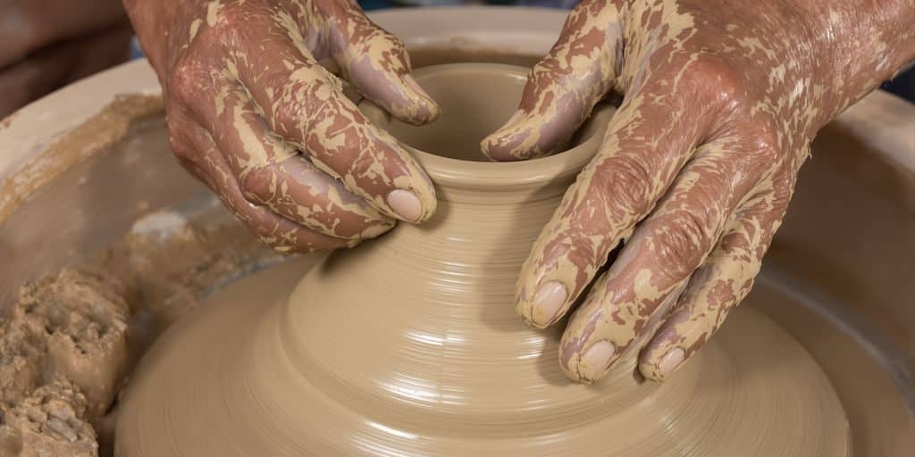 Mains travaillant l'argile pour créer une poterie ornée.