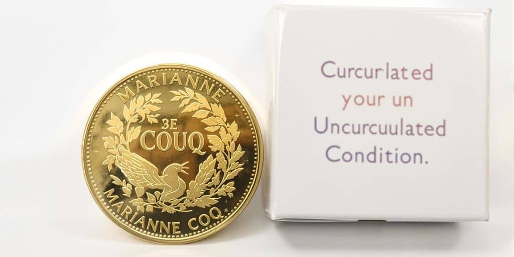 Une pièce Marianne Coq dorée et sa boîte scellée.