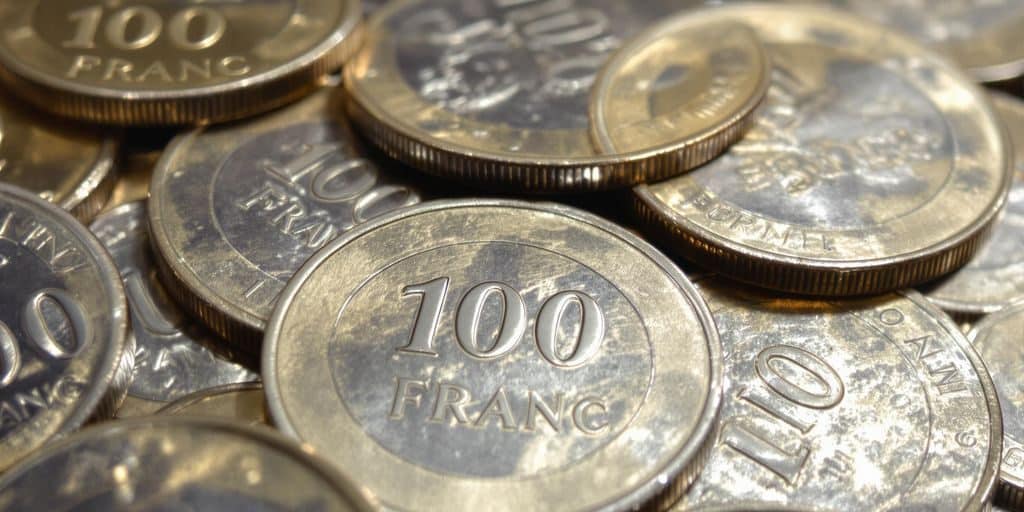 Gros plan de pièces de 100 francs en argent, reflets dorés.