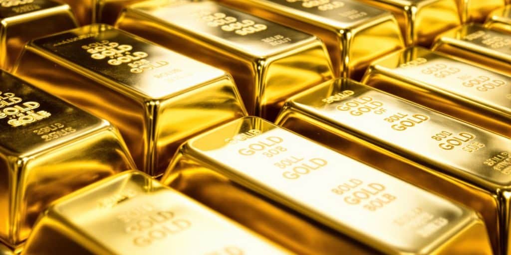 Lingots d'or brillants empilés sur une surface réfléchissante.