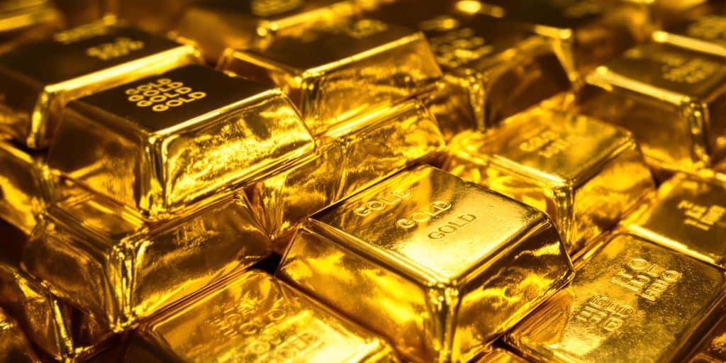Lingots d'or brillants empilés sur une surface réfléchissante.