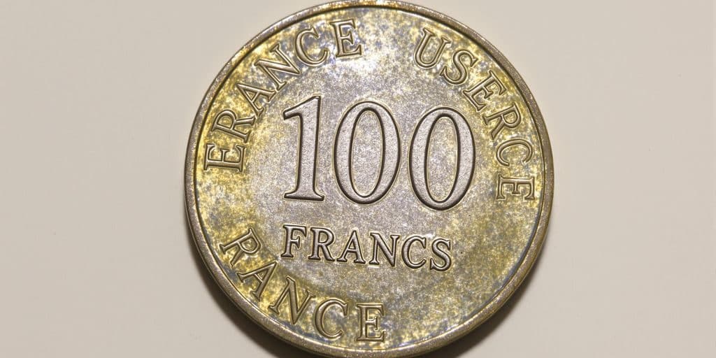 Une pièce de 100 francs en argent brille sous la lumière.